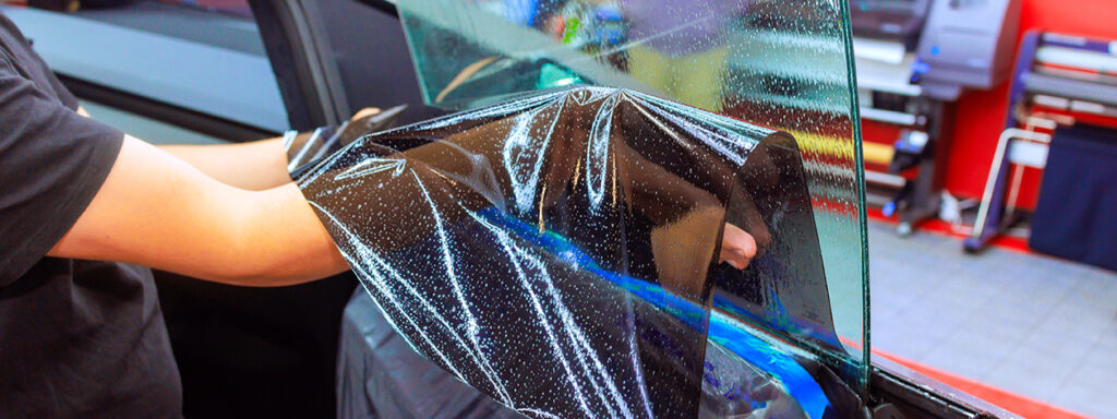 Our Night Shift Tint technician applies window tint to a car door, ensuring a perfect fit.
